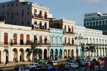 Classic American cars parked in front of colorful colonial buildings with arcades in Havana